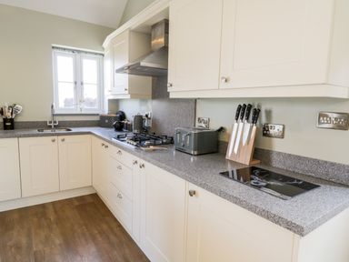 A kitchen with white cabinets a gas stove a knife set a toaster and a window at Stag Cottage at Broadings Farm Whitby