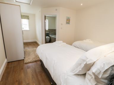 A bedroom with two single beds white bedding wooden floor a rug a wardrobe and an en suite bathroom at Stag Cottage at Broadings Farm Whitby