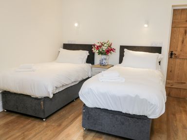 A bedroom with two single beds white bedding a wooden door and flowers on a nightstand at Stag Cottage at Broadings Farm in Whitby