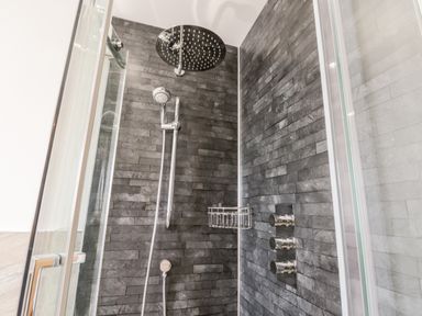 A shower area with dark gray tiled walls glass doors and chrome fixtures at Stag Cottage at Broadings Farm in Whitby