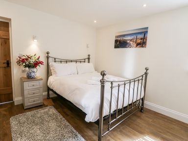 A bedroom with a metal bed frame white bedding bedside table with flowers and a beach picture on the wall at Stag Cottage at Broadings Farm in Whitby