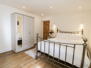 A bedroom with a metal bed frame white bedding a wardrobe with a mirror on door a wooden door a nightstand with flowers and a rug on wooden floor at Stag Cottage at Broadings Farm Whitby