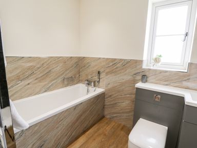 A bathroom with a bathtub and a toilet under a window at Stag Cottage at Broadings Farm in Whitby