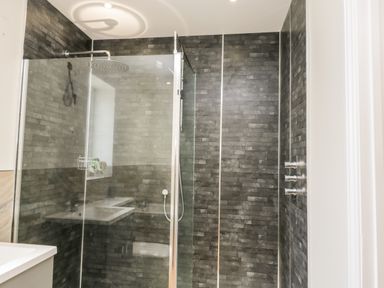 A shower area with glass doors dark tiled walls and a rain showerhead at Stag Cottage at Broadings Farm in Whitby