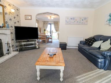A living room with a blue sofa wooden coffee table a television and a view to dining area at Rhiangwyn in Llanrhyddlad near Cemaes Bay