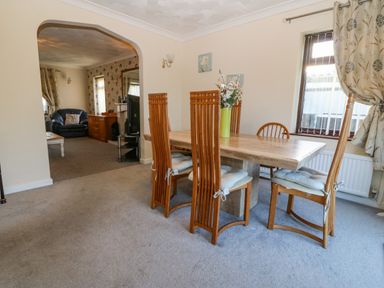 A dining area with wooden chairs and a table with a vase of flowers next to a window with curtains at Rhiangwyn in Llanrhyddlad near Cemaes Bay