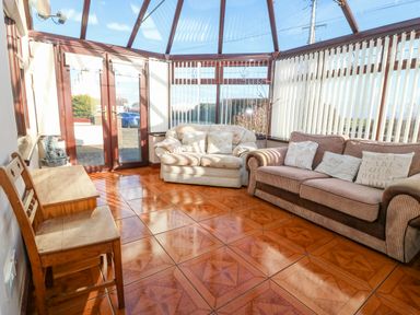 A conservatory with two sofas a wooden chair and a storage box at Rhiangwyn in Llanrhyddlad near Cemaes Bay
