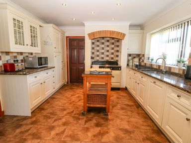 A kitchen with white cabinets a wooden island a stove under a tiled arch and a window with vertical blinds at Rhiangwyn Llanrhyddlad near Cemaes Bay