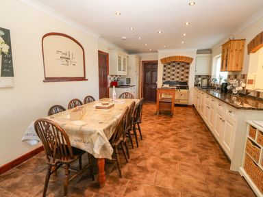 A kitchen with a long table and chairs a stove and cabinets at Rhiangwyn in Llanrhyddlad near Cemaes Bay