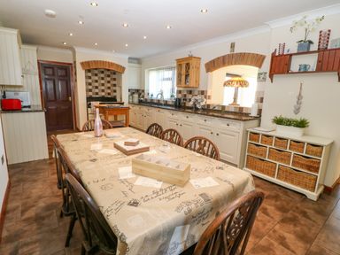 A kitchen with a dining table covered with a tablecloth and wooden chairs at Rhiangwyn in Llanrhyddlad near Cemaes Bay