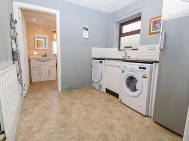 A laundry room with washing machine dryer sink and fridge near a bathroom at Rhiangwyn in Llanrhyddlad near Cemaes Bay