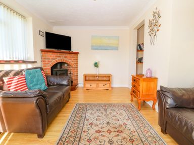 A living room with two leather sofas a brick fireplace a wooden TV stand and an orange side table with a vase on it at Rhiangwyn in Llanrhyddlad near Cemaes Bay