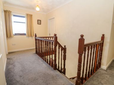 A stairwell with wooden banisters and a window with beige curtains at Rhiangwyn in Llanrhyddlad near Cemaes Bay