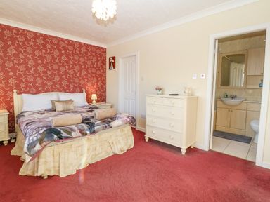 A bedroom with a bed beside two nightstands a dresser and an ensuite bathroom at Rhiangwyn in Llanrhyddlad near Cemaes Bay
