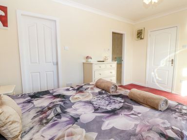 A bedroom with floral bedspread two rolled towels on the bed white dresser and two white doors at Rhiangwyn in Llanrhyddlad near Cemaes Bay