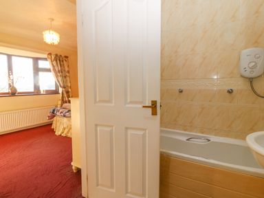 A bathroom with a bathtub and beige tiles next to a bedroom with red carpet and a window at Rhiangwyn in Llanrhyddlad near Cemaes Bay