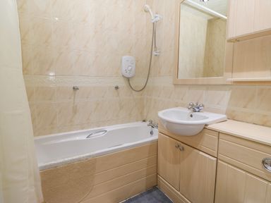 A bathroom with a bathtub shower sink and wooden cabinets at Rhiangwyn in Llanrhyddlad near Cemaes Bay