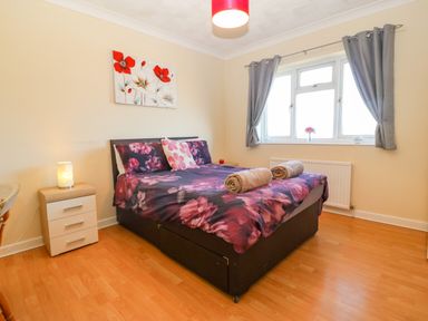 A bedroom with a double bed with floral bedding two rolled towels on the bed bedside tables a lamp window with grey curtains and wooden flooring at Rhiangwyn in Llanrhyddlad near Cemaes Bay