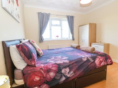A bedroom with a bed covered in floral bedding two rolled towels on the bed a wardrobe and chest of drawers near the window at Rhiangwyn in Llanrhyddlad near Cemaes Bay
