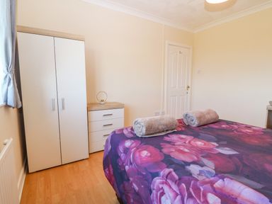 A bedroom with a bed covered in a floral bedspread with two rolled towels on it and a white wardrobe and chest of drawers near the door at Rhiangwyn in Llanrhyddlad near Cemaes Bay