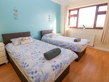 A bedroom with two single beds with floral bedding and rolled towels on a wooden floor at Rhiangwyn in Llanrhyddlad near Cemaes Bay