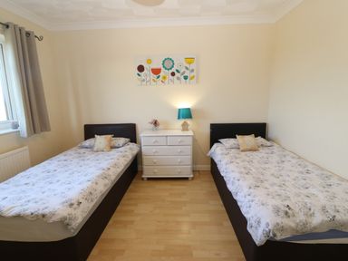 A bedroom with two single beds and a white dresser with a lamp and flowers on it at Rhiangwyn in Llanrhyddlad near Cemaes Bay