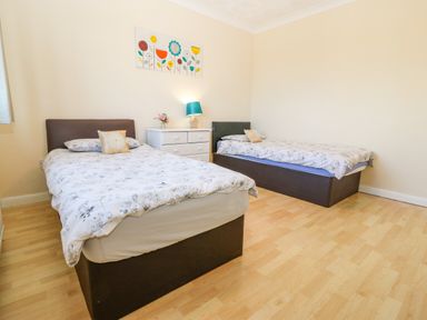 A bedroom with two single beds a white dresser with a lamp and flower painting on the wall at Rhiangwyn in Llanrhyddlad near Cemaes Bay