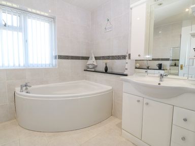 A bathroom with a corner bathtub a sink with cabinet a window with blinds and a mirror at Rhiangwyn in Llanrhyddlad near Cemaes Bay