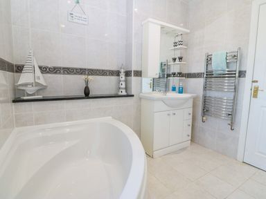 A bathroom with a bathtub a sink with a cabinet a heated towel rail and decorative items at Rhiangwyn in Llanrhyddlad near Cemaes Bay