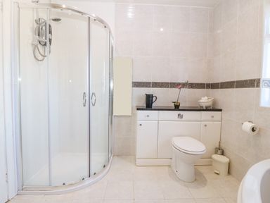 A bathroom with a curved glass shower enclosure a toilet and a cabinet with a black countertop and decorative items at Rhiangwyn in Llanrhyddlad near Cemaes Bay