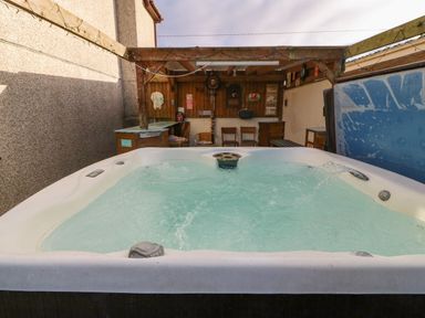 An outdoor hot tub with bubbling water under a wooden pergola with chairs and decorations at Rhiangwyn in Llanrhyddlad near Cemaes Bay