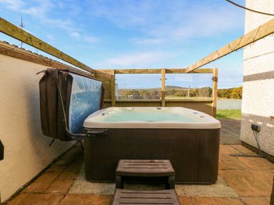 An outdoor hot tub with steps on a paved patio with wooden fencing and a view of greenery at Rhiangwyn in Llanrhyddlad near Cemaes Bay