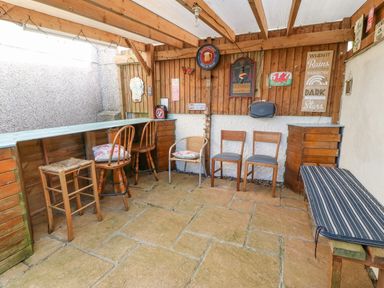 An outdoor patio area with a wooden bar counter and various chairs against wooden walls with decorations at Rhiangwyn in Llanrhyddlad near Cemaes Bay