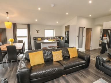 An open plan living room and kitchen with black leather sofas yellow cushions dining table and chairs and kitchen island at Box Tree Escapes in Kirkby Lonsdale