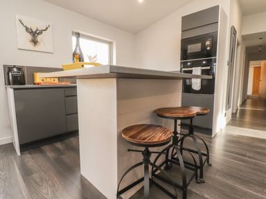 A kitchen with a countertop island and three wooden stools with black metal legs at Box Tree Escapes in Kirkby Lonsdale