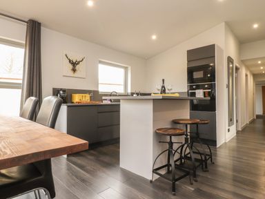 A kitchen with a breakfast bar and stools a dining table with chairs and a painting of a stag at Box Tree Escapes in Kirkby Lonsdale