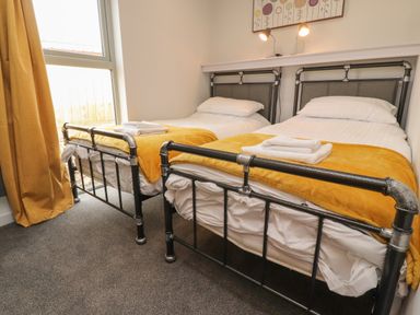 A bedroom with two single beds with yellow blankets and white towels on each bed at Box Tree Escapes in Kirkby Lonsdale