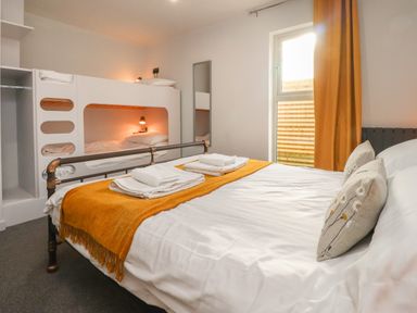 A bedroom with a double bed and bunk beds with orange throw and curtains at Box Tree Escapes in Kirkby Lonsdale