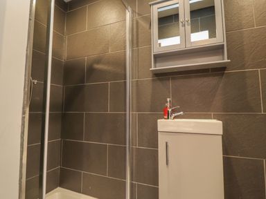A bathroom with a shower area with dark tiles and a white sink cabinet with a mirror cabinet above at Box Tree Escapes in Kirkby Lonsdale
