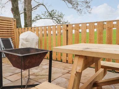An outdoor patio area with a wooden table and bench a metal fire pit and wooden fencing at Box Tree Escapes in Kirkby Lonsdale