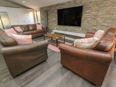 A living room with three brown leather sofas pink cushions a wooden coffee table and a wall mounted tv at Box Tree Escapes in Wennington near Kirkby Lonsdale