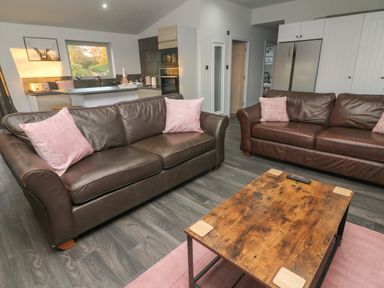 A living area with two brown leather sofas with pink cushions and a wooden coffee table at Box Tree Escapes in Wennington near Kirkby Lonsdale