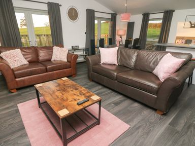A living room with two leather sofas a wooden coffee table a pink rug and dining area visible at Box Tree Escapes Wennington near Kirkby Lonsdale