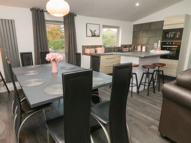 A dining area with a gray table and black chairs next to a kitchen with a breakfast bar and stools at Box Tree Escapes in Wennington near Kirkby Lonsdale