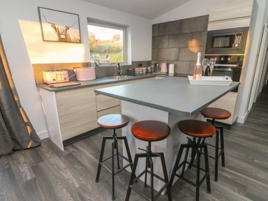 A kitchen with a countertop island with four stools and appliances at Box Tree Escapes Wennington near Kirkby Lonsdale