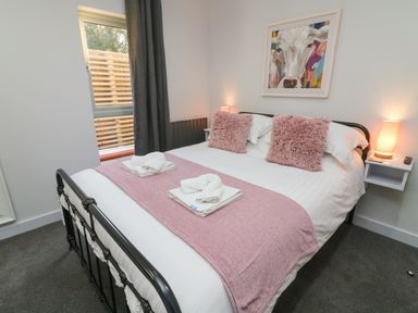 A bedroom with a black metal bed frame two pink pillows a pink throw blanket and white towels with a painting of a cow above the bed at Box Tree Escapes in Wennington near Kirkby Lonsdale