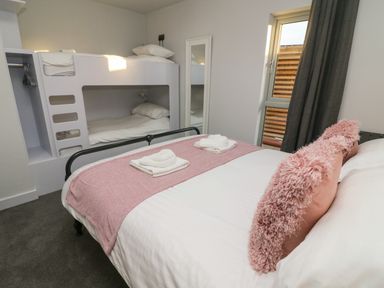 A bedroom with a double bed with pink pillows and folded towels a bunk bed a mirror and a window with curtains at Box Tree Escapes in Wennington near Kirkby Lonsdale
