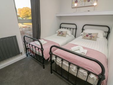 A bedroom with two single beds with black metal frames and pink throws at Box Tree Escapes in Wennington near Kirkby Lonsdale