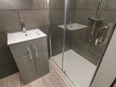 A bathroom with a gray sink cabinet and a glass enclosed shower at Box Tree Escapes Wennington near Kirkby Lonsdale