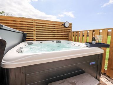 An outdoor hot tub with bubbling water and a tray holding a bottle and glasses at Box Tree Escapes Wennington near Kirkby Lonsdale